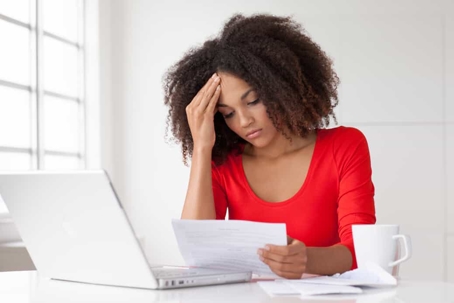 Stressed young woman sits at a desk with her laptop and coffee reviewing documents