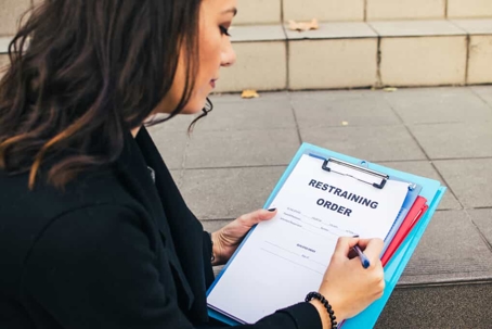 Woman with dark hair sits outside as she fills out the paperwork for a restraining order