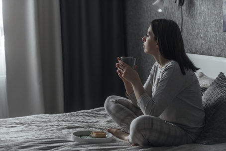 Sad woman sitting on bed drinking coffee